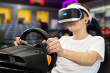 Teenage Boy Wearing Virtual Reality Glasses, Who Holds On To The Steering Wheel And Plays A Computer Game On The Console