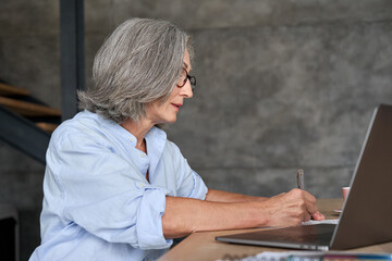 Wall Mural - mature adult 60s business woman working at laptop watching videoconference webinar. business lady e 
