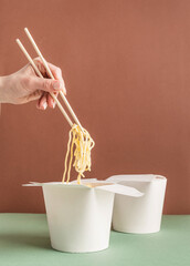 Opened WOK paper box for mock up design. Woman hand holding noodles with chopsticks