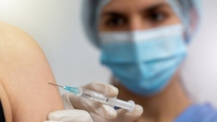 Female doctor with surgical mask giving injection to person