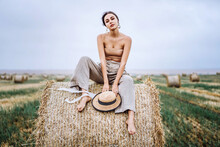 Smiling Woman In Sunglasses With Bare Shoulders On A Background Of Wheat Field And Bales Of Hay.