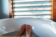 Bathtub feet soaking in warm water woman taking a warm bath at luxury bathroom villa. Window view.
