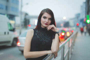 Poster - Young brunette female in a leather jacket posing leaning on a railing in a street