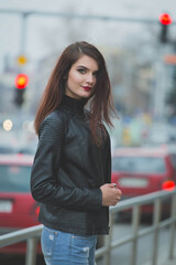 Poster - Vertical shot of a young brunette female in a leather jacket posing on a railing in the street