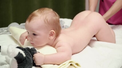 the masseuse gives a leg massage to a happy child (boy). the baby lies on his belly, holds a soft to
