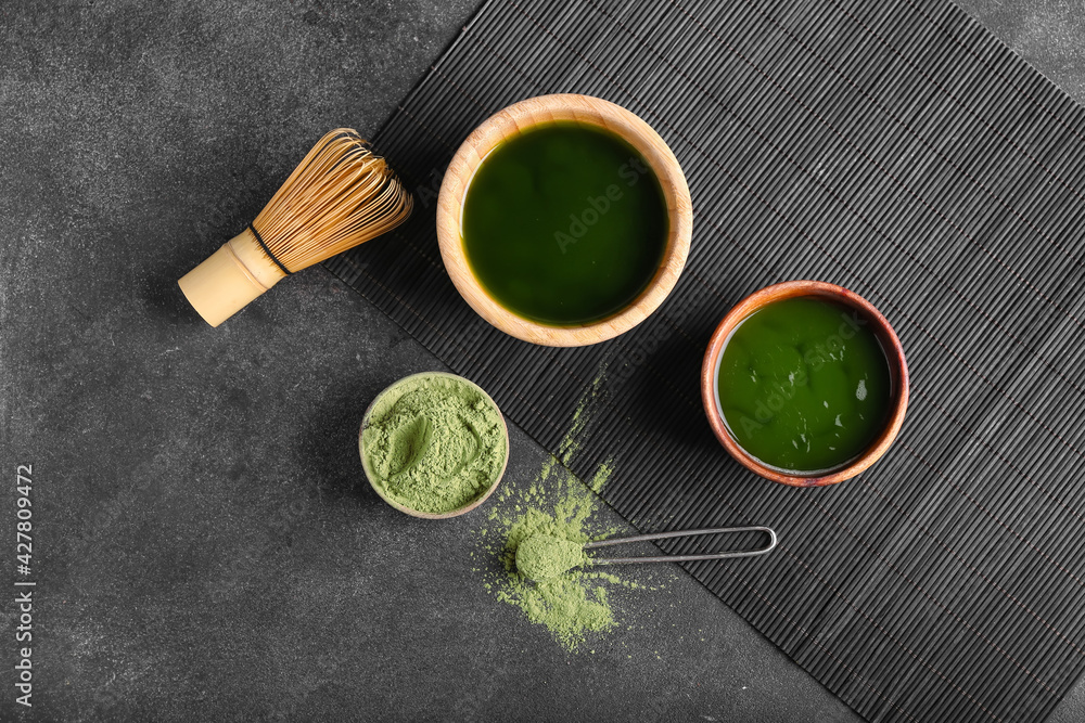 Bowls with matcha tea, powder and chasen on dark background