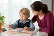 © Tomsickova - Cute preschool child, blond boy, filling some homework in a work book and coloring, mother helping him