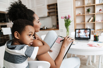 Wall Mural - Black boy hugging his mother while she working with laptop at home