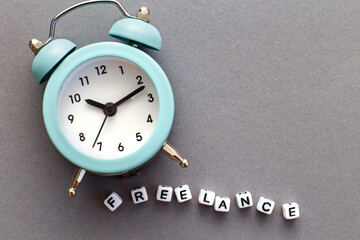 Alarm clock and word freelance made from plastic cubes of beads on gray background