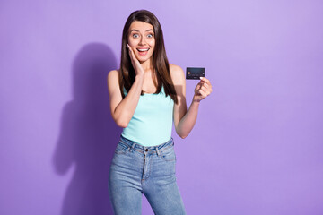 Sticker - Photo of amazed charming young woman hold hands cheekbone debit card isolated on violet color background