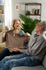 Wall Mural - Elderly woman giving a gift to her husband. Senior woman showing a shirt she bought for her husband