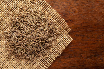 Wall Mural - Macro close-up of Organic cumin seed (Cuminum cyminum) or jeera on the wooden top background and jute mat. Pile of Indian Aromatic Spice. Top view