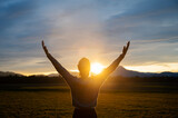 Fototapeta  - Woman embracing life standing outside in beautiful meadow with her arms raised high