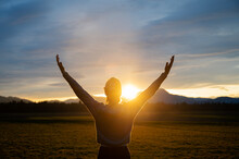 Woman Embracing Life Standing Outside In Beautiful Meadow With Her Arms Raised High