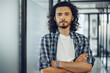 © fotofabrika - Portrait of young curly casually dressed male entrepreneur standing in a glass corridor