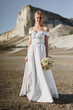 © fotofabrika - Beautiful bride in a wedding dress with a bouquet standing against white rock