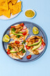 Tacos with crispy fish, avocado, guacamole sauce, nachos chips and lime on blue background. Top view. Mexican cuisine