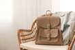 © New Africa - Stylish beige backpack and jacket on wicker chair indoors, space for text
