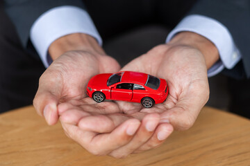 Wall Mural - Businessman hand holding red car toy on table. Financial, money, refinance and Car insurance concept