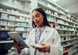 © StratfordProductions - Woman in chemist wearing labcoat checking medicine details in digital tablet