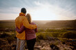 © StratfordProductions - Rear view of young couple in love embracing while looking at beautiful sunrise after hiking to mountain cliff edge