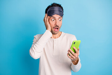 Poster - Photo portrait of shocked astonished guy with open mouth touching face holding phone in one hand isolated on vivid blue colored background