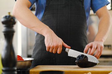 Wall Mural - The male Caucasian chef cuts vegetables, peppers, tomatoes and eggplants on a wooden cutting board.