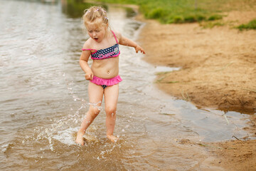 little cute girl have fun playing with a spray of water in the river at summer. copy space