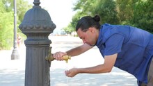 Man Stand Stooping Against Street Fountain Flatten Hair By Hand And Drink Water