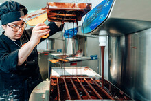 Woman Chocolatier At The Chocolate Machine In Her Workshop. Artisanal Business Equipment Technology Machinery.