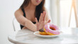 © KomootP - Close up female hand pushing out avoid say no her favorite donut sweets for good health and weight control as diet and healthy concept