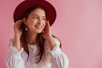 Happy smiling elegant girl wearing stylish burgundy color hat, pearl earrings, vintage blouse, posing on pink background. Women`s fashion conception. Copy, empty space for text
