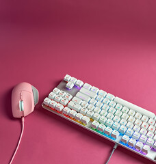 A set of gaming accessories for gaming. Stylish gaming pink mouse and white keyboard with RGB light. Keyboard and mouse with colorful backlight on pink background