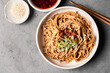 © The Picture Pantry - Spicy sesame noodles in a bowl next to chile oil and sesame seeds.