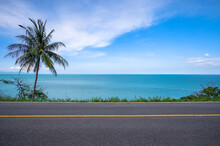 Coconut Palm Tree On Side Of Asphalt Road And Tropical Seascape Scenery In The Background.