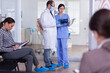 © DC Studio - Dentist in stomatology waiting area holding patient x-ray explaining diagnosis to nurse in a crowded hallway with patient filling form. Dentistiry staff in reception.