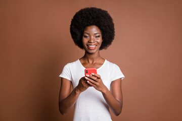 Sticker - Photo of cheerful lady hold telephone look camera wear white t-shirt isolated brown color background