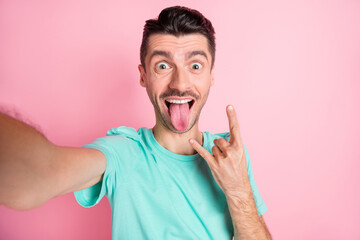 Sticker - Photo of young funny cheerful crazy man stick tongue out take selfie show rock n roll sign isolated on pink color background