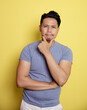 © Odua Images - casual young man smile thinking idea with holding the chin and one hand on stomach isolated on a yellow color background