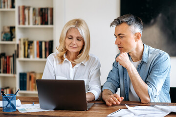 Business meeting in the office. Mature successful two business partners in stylish clothes are sitting at the table, working on a new start up, discussing work issues, writing down ideas in a laptop