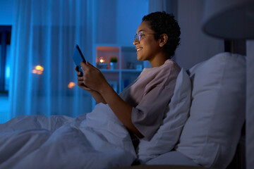 Wall Mural - technology, internet and people concept - happy smiling young african american woman with tablet pc computer lying in bed at home at night