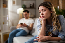 Couple At Home After Having A Fight. Sad Depressed Woman Sitting On Sofa