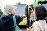 Fototapeta Kuchnia - a woman in a headscarf with a finger pointing towards the bus while talking to a woman with headphones while going by bus
