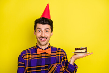 Poster - Photo of young man happy positive smile lick lips tasty delicious cake wear party hat isolated over yellow color background