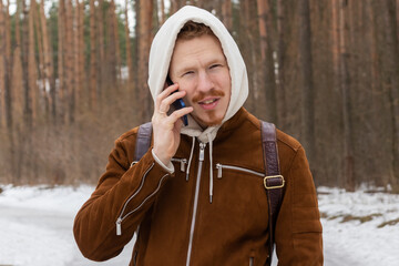 a guy in a white hood is talking on the phone outside in early spring