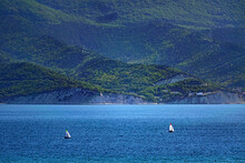 Dark Blue Sea By A High Green Mountain With Two Sailboats