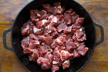 Raw meat is cut into pieces in a pan. Isolated on wood table background. Top view.