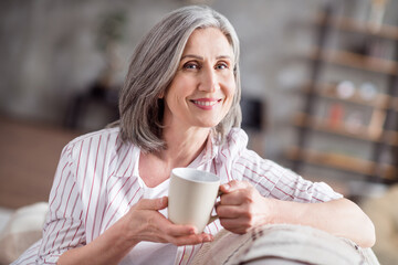 Photo of happy cheerful positive old lady good mood hold hands mug weekend indoors inside house home