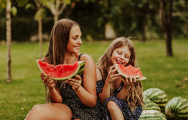 Two young pretty girls sitting on bunch of watermelons and eating slices of it.