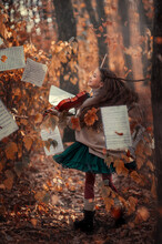 A Beautiful Girl Plays The Violin Among The Autumn Orange Foliage In The Forest And With Music Sheets In The Background.